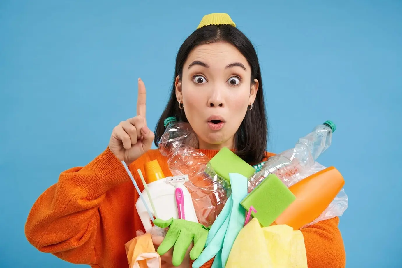 Nahes Porträt einer asiatischen Frau, die nach oben zeigt, ein Banner präsentiert und Recyclinggegenstände hält – leere Plastikbo.