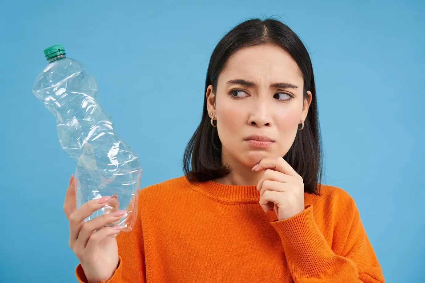 Porträt einer besorgten, nachdenklichen Frau, die eine leere Plastikflasche ansieht und darüber nachdenkt, wie sie recycelt werden kann.